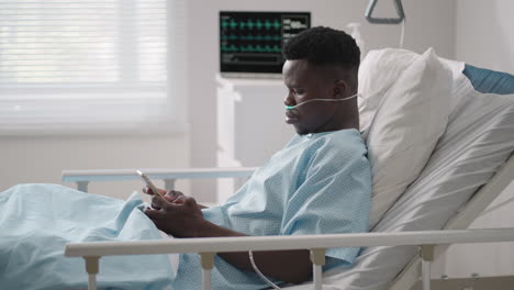 Afrikanischer-Männlicher-Patient-Benutzt-Smartphone,-Während-Er-Im-Bett-Liegt.-Afrikanischer-Patient,-Der-Im-Krankenzimmer-Telefoniert